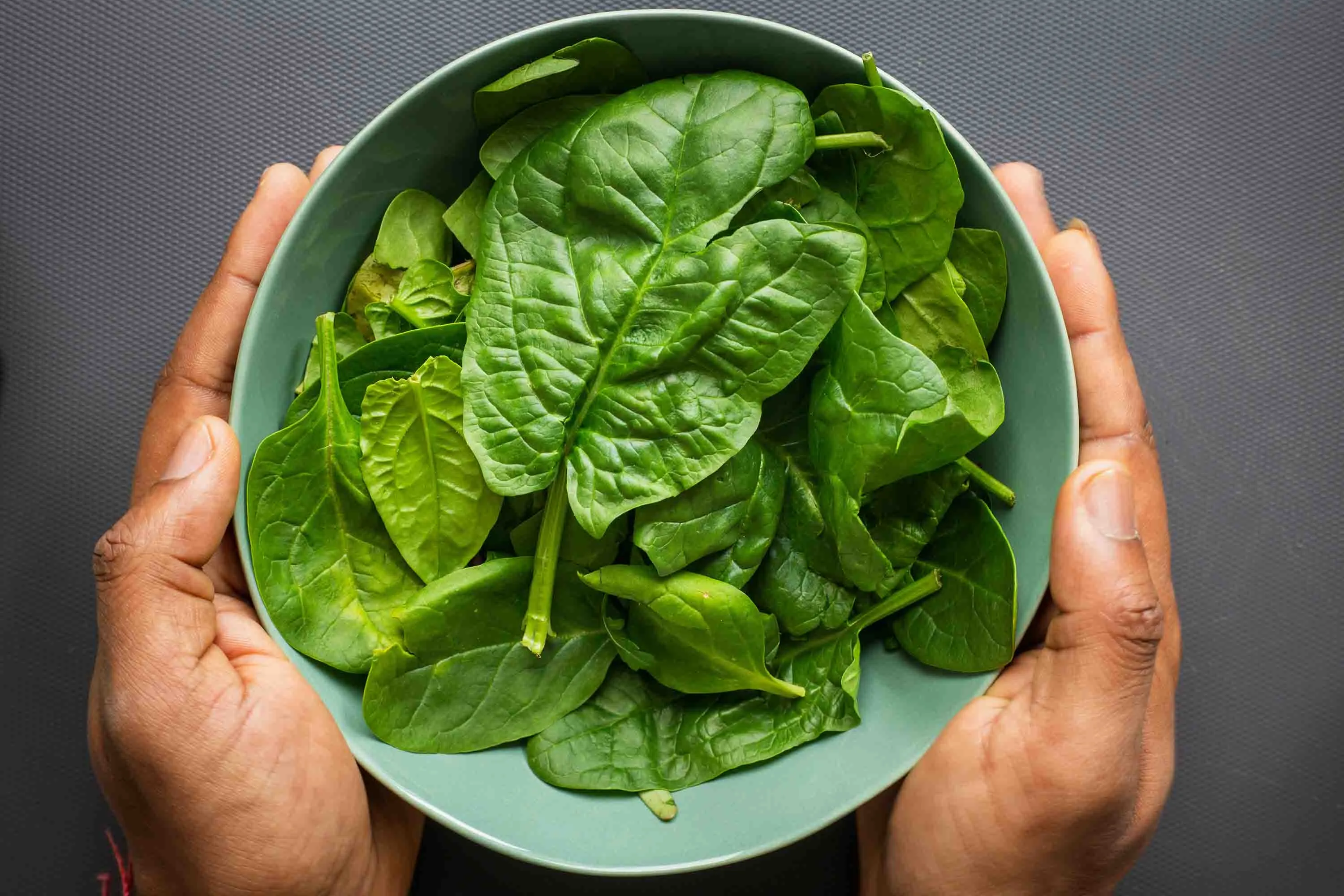 Hands holding fresh spinach leaves, illustrating vitamin K2’s crucial role in directing calcium to bones and teeth—especially when paired with vitamin D3 (cholecalciferol) for optimal health.