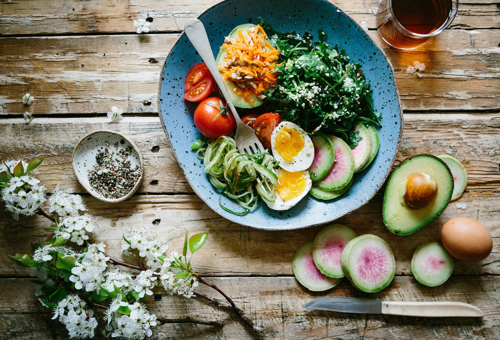 A rustic wooden table topped with a colorful plate of vegetables, sliced boiled eggs, and avocado, illustrating a balanced meal that supports healthy blood sugar control.
