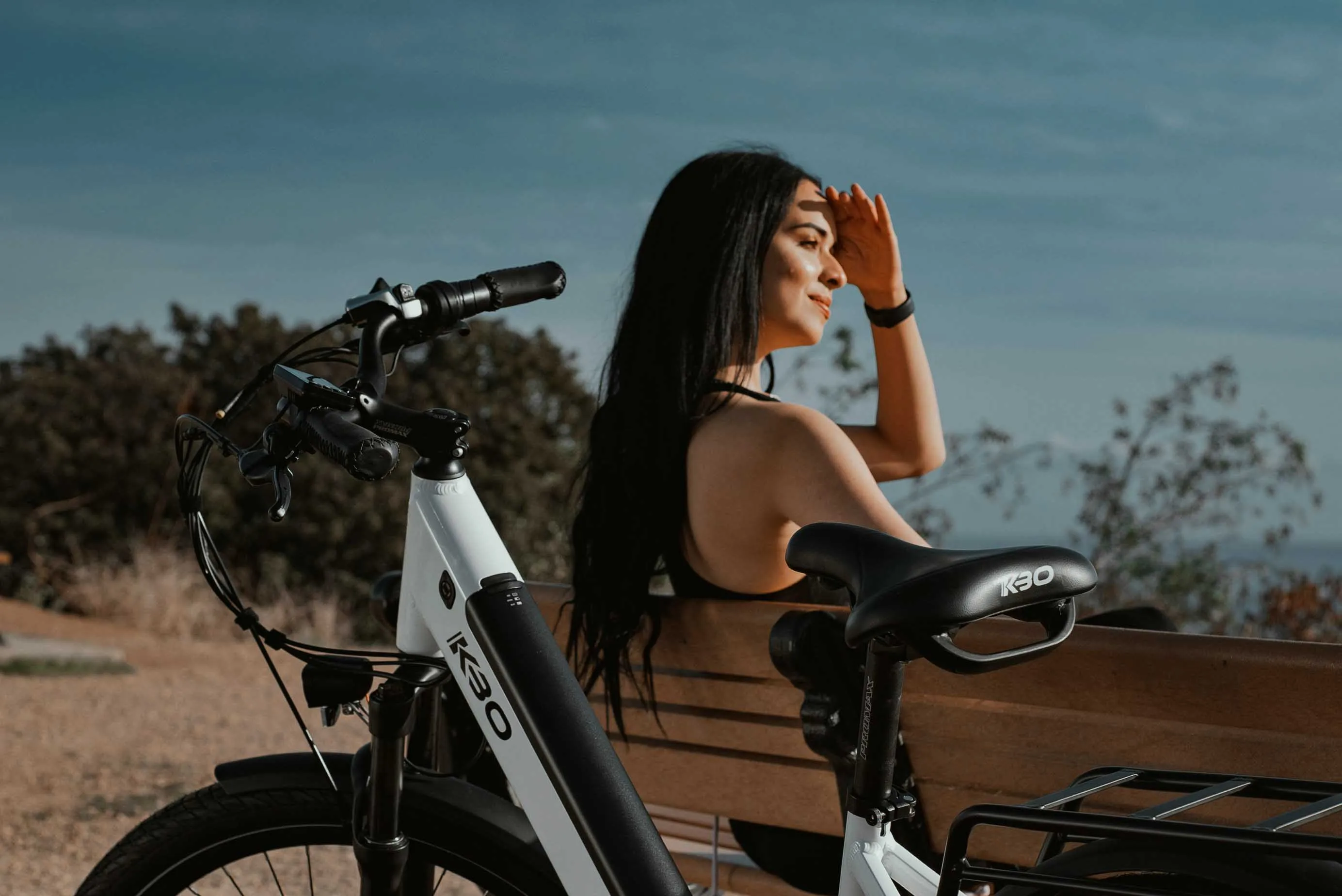 Woman in a black athletic outfit sits on a bench next to an electric bike under bright sunlight, illustrating the benefits of natural vitamin D from sun exposure and an active, healthy lifestyle.