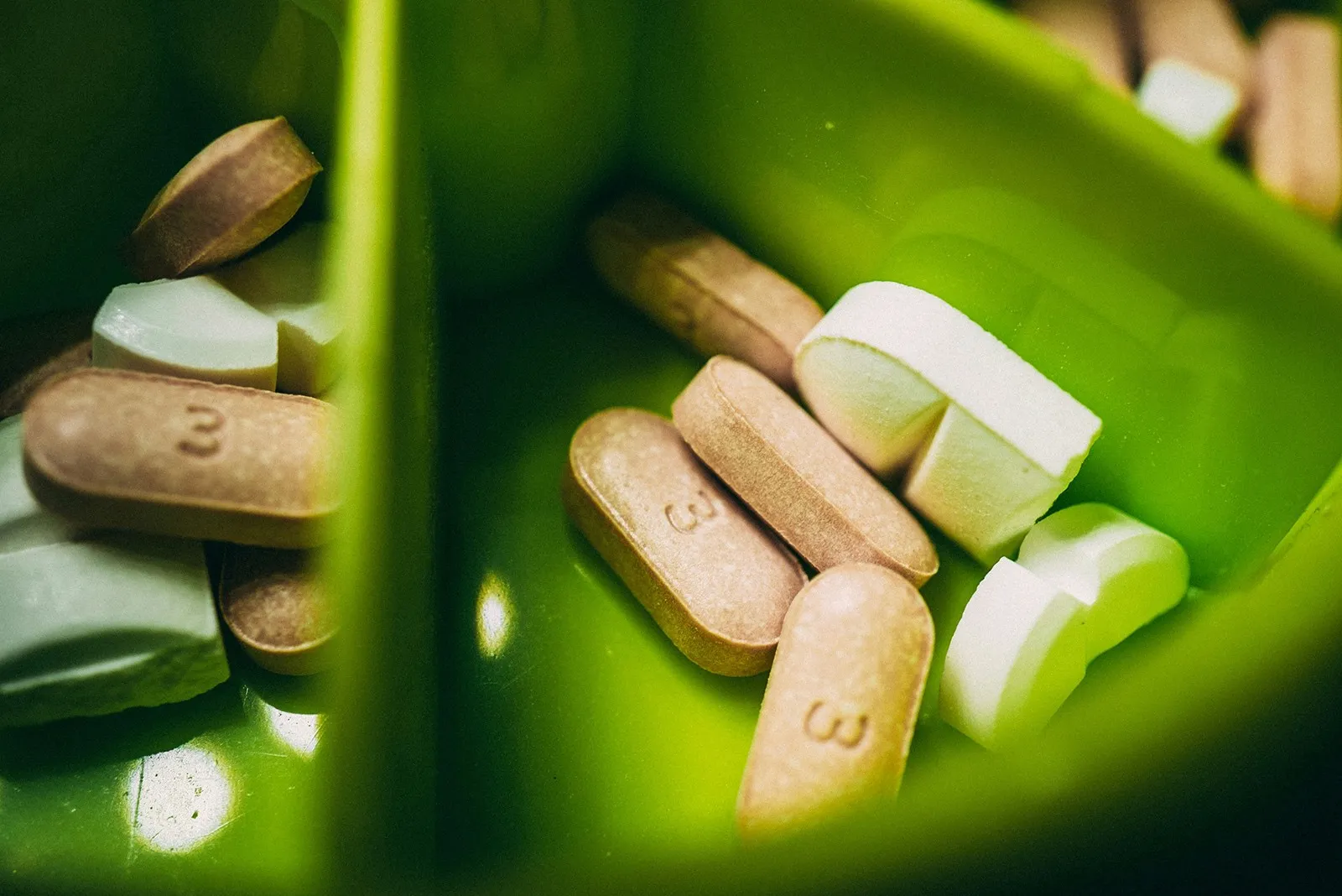 Various supplements and vitamins in a green pill organizer, illustrating sleep-supporting nutrients like magnesium or GABA.