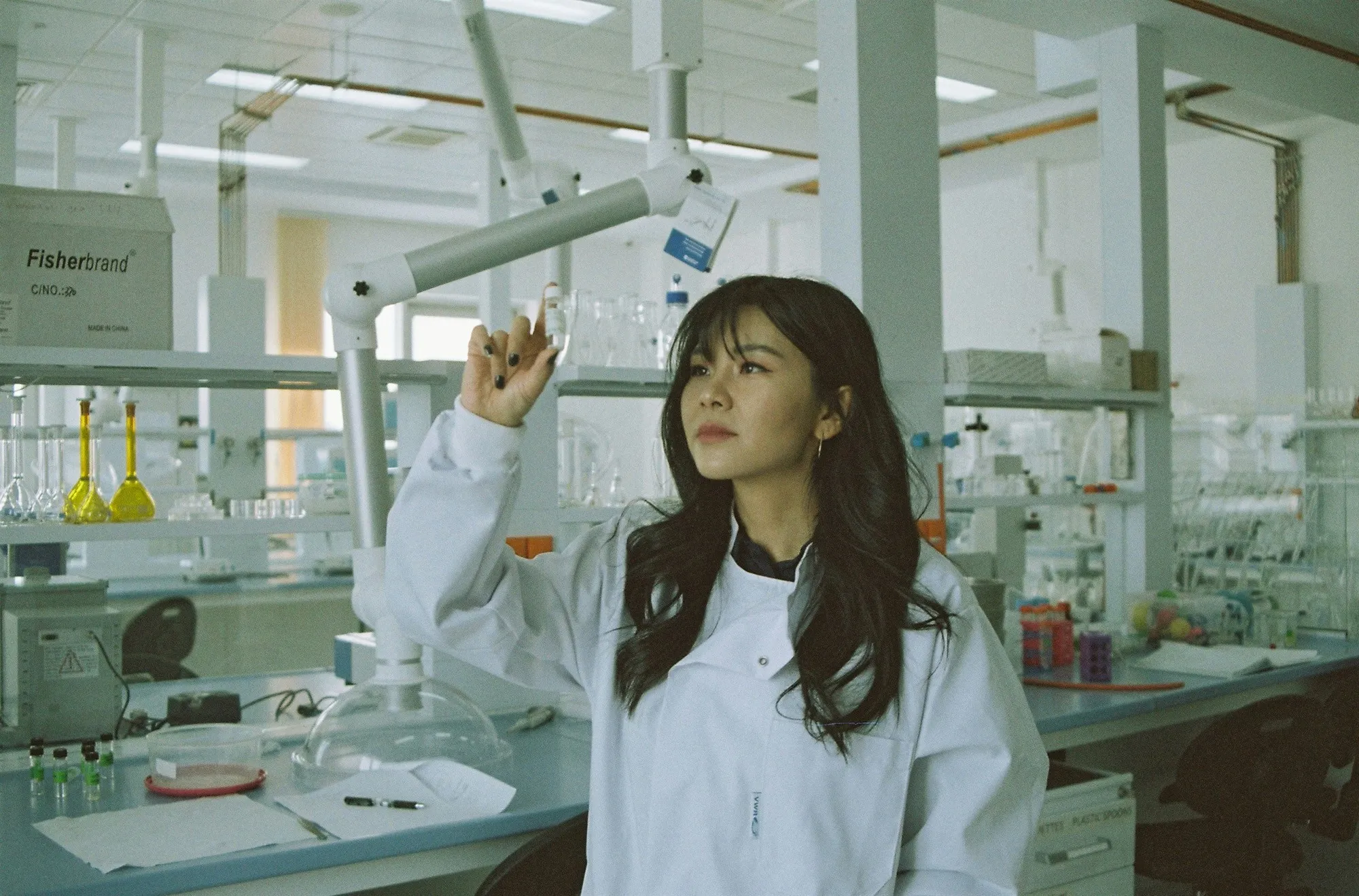 A female researcher in a white lab coat examines a small vial in a modern laboratory, representing advanced diagnostic testing for biomarkers like HbA1c.