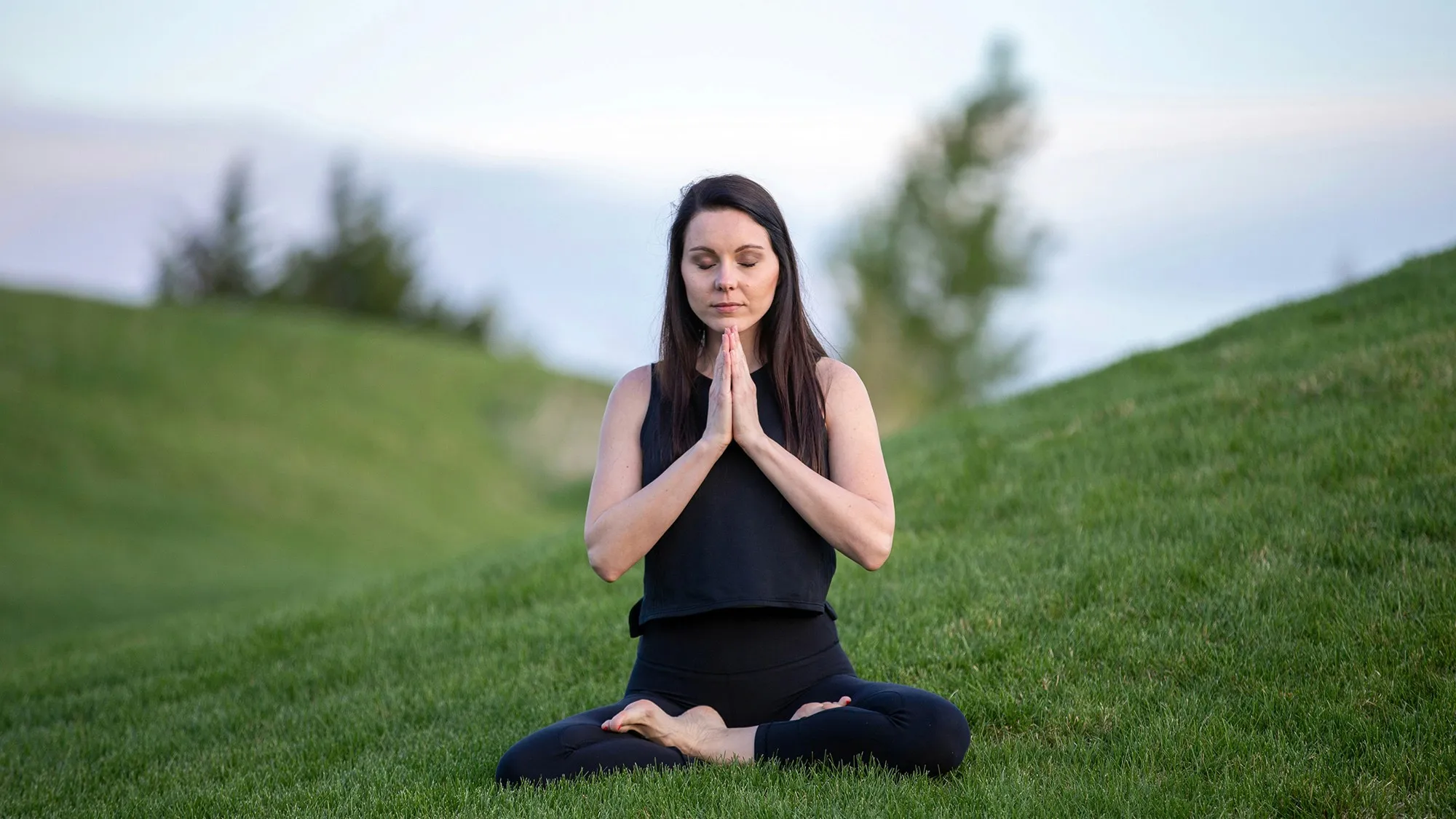 A woman practicing mindfulness meditation on a grassy hill to help manage perimenopause symptoms by balancing estrogen and progesterone levels.